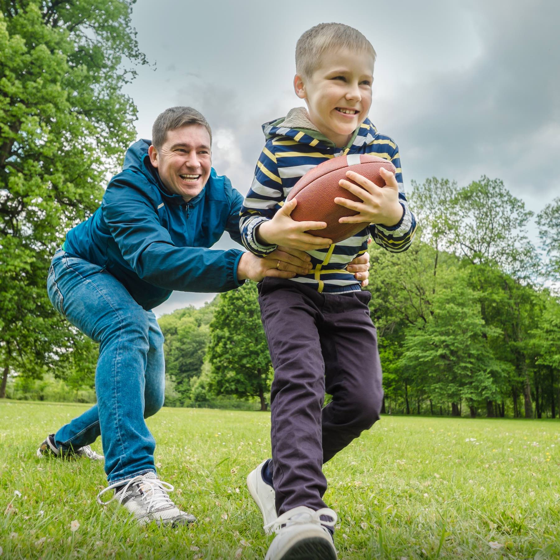 Father and son playing football, Father's day, Playful Man teaching Boy rugby outdoors in sunny day at public park. Family sports weekend.