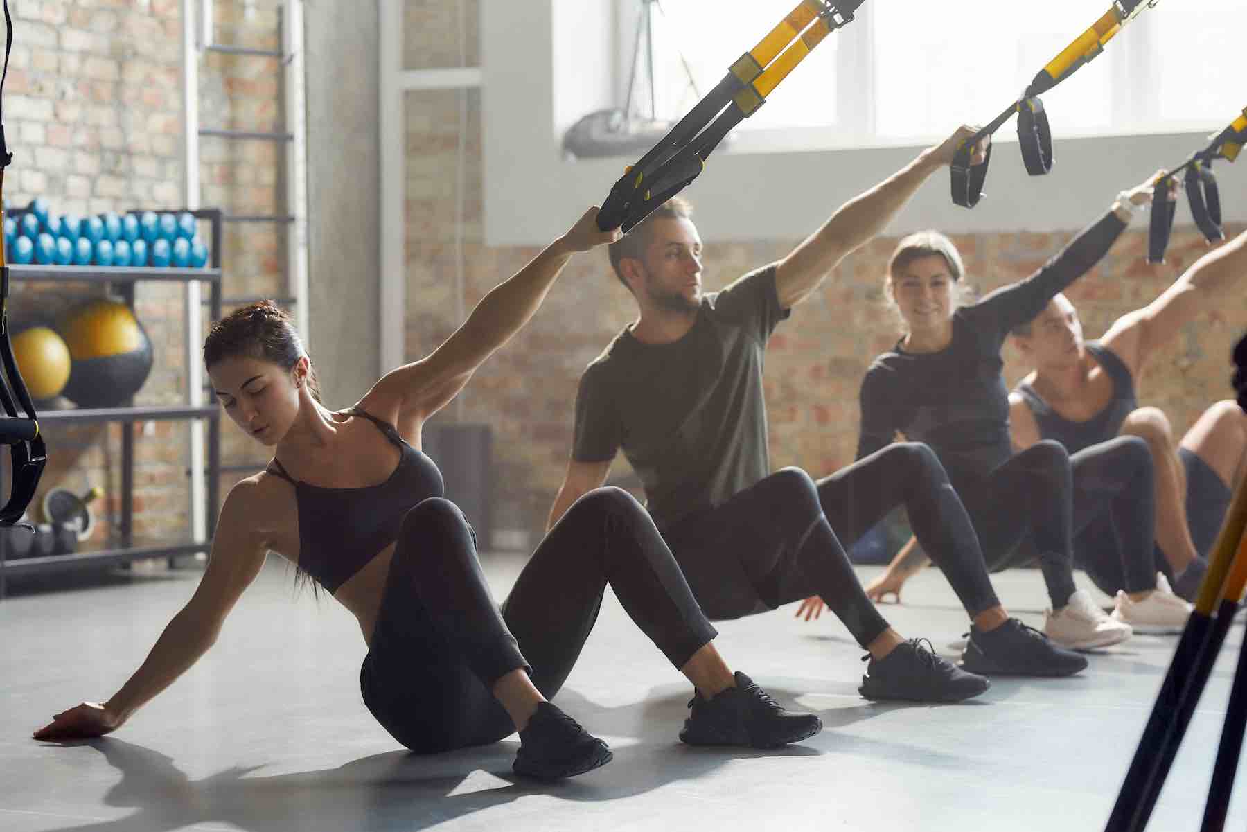 Full-length shot of men and women doing fitness TRX training exercises at industrial gym. Push-up, crossfit group workout concept. Horizontal shot. Selective focus