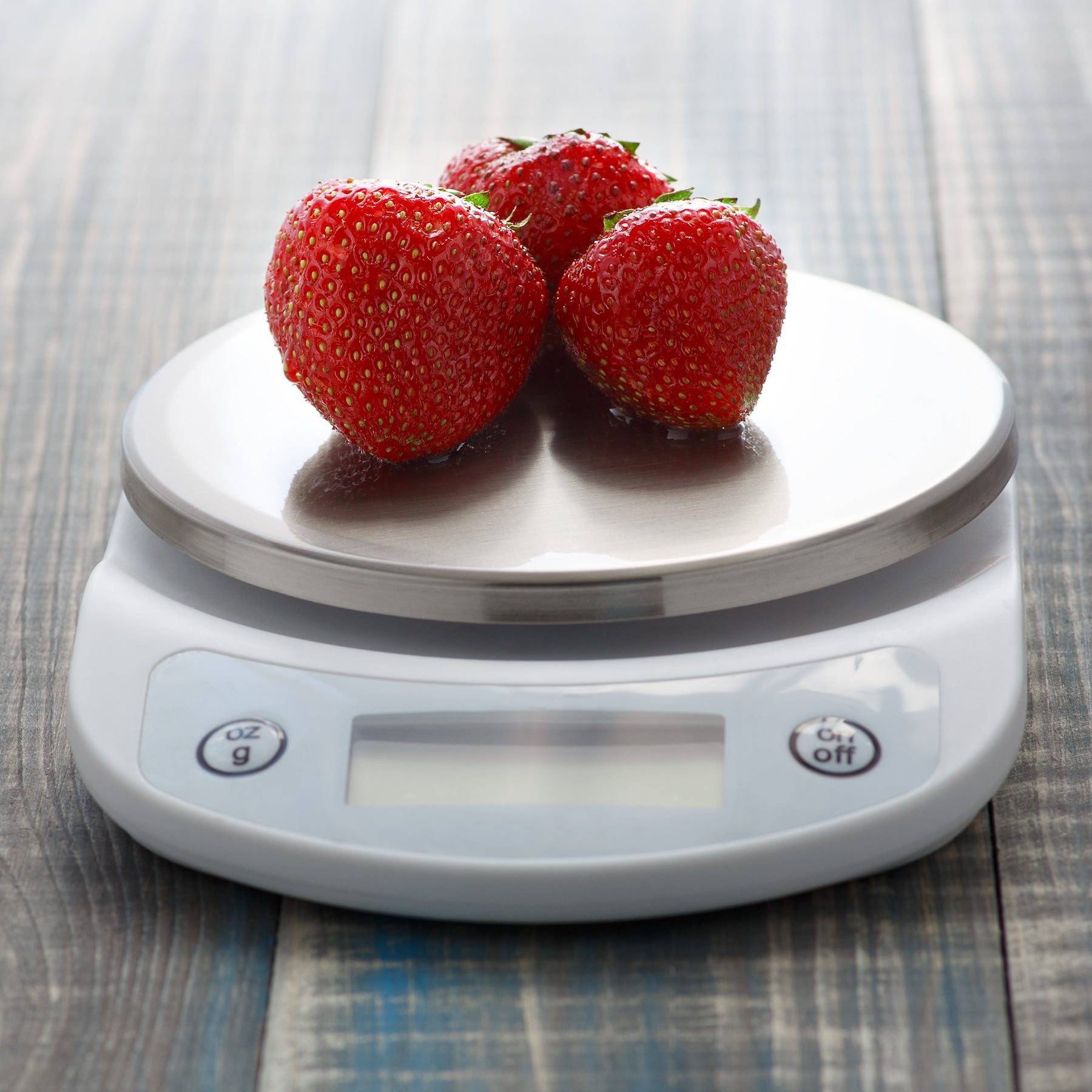 Three ripe washed strawberries lie on digital kitchen scales