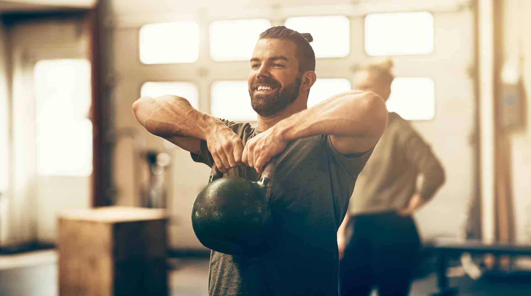 Fit young man in sportswear smiling and lifting dumbells during an exercise class in a gym