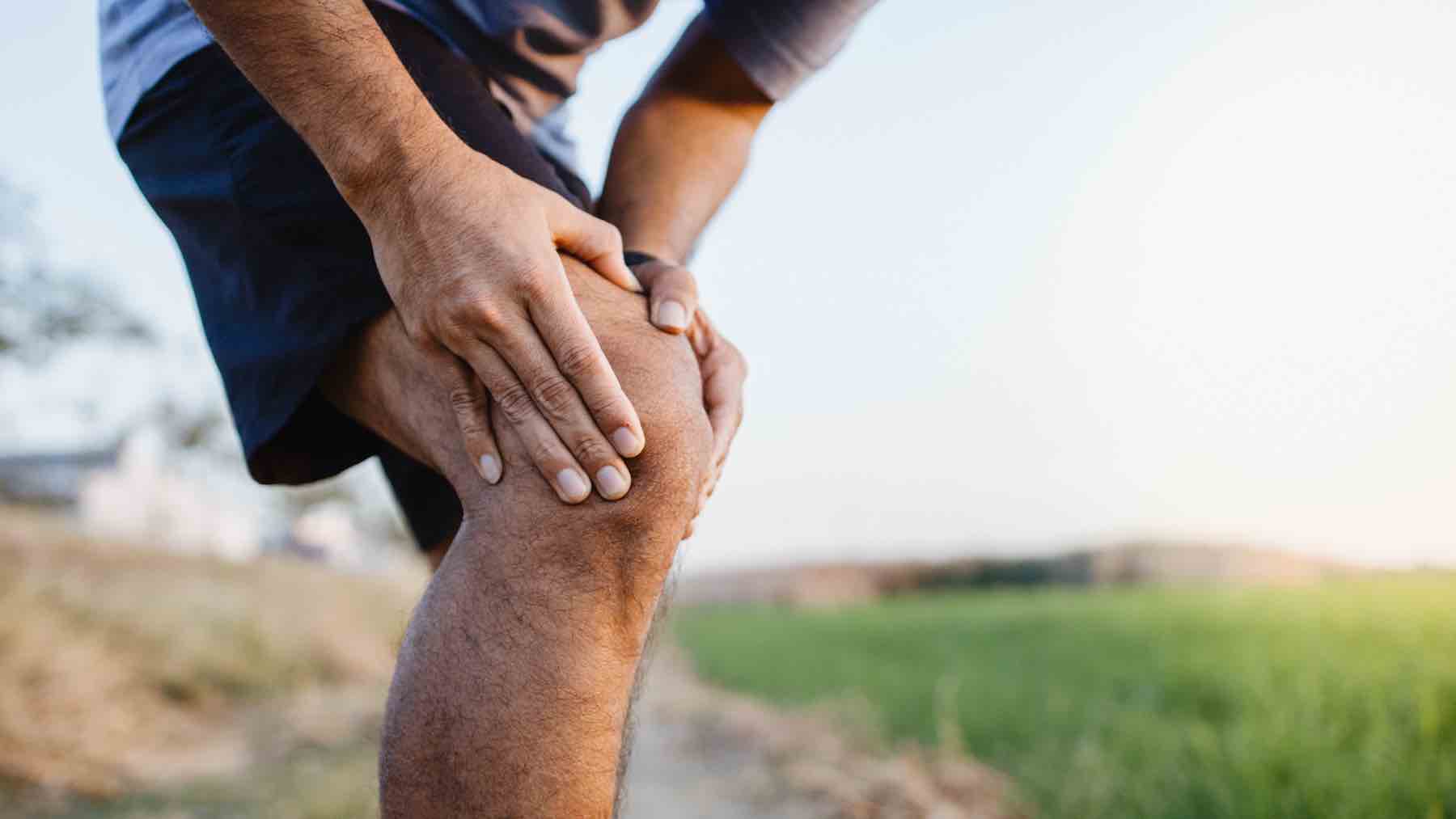 Sporty man in pain after sustaining a knee injury during a running training session.