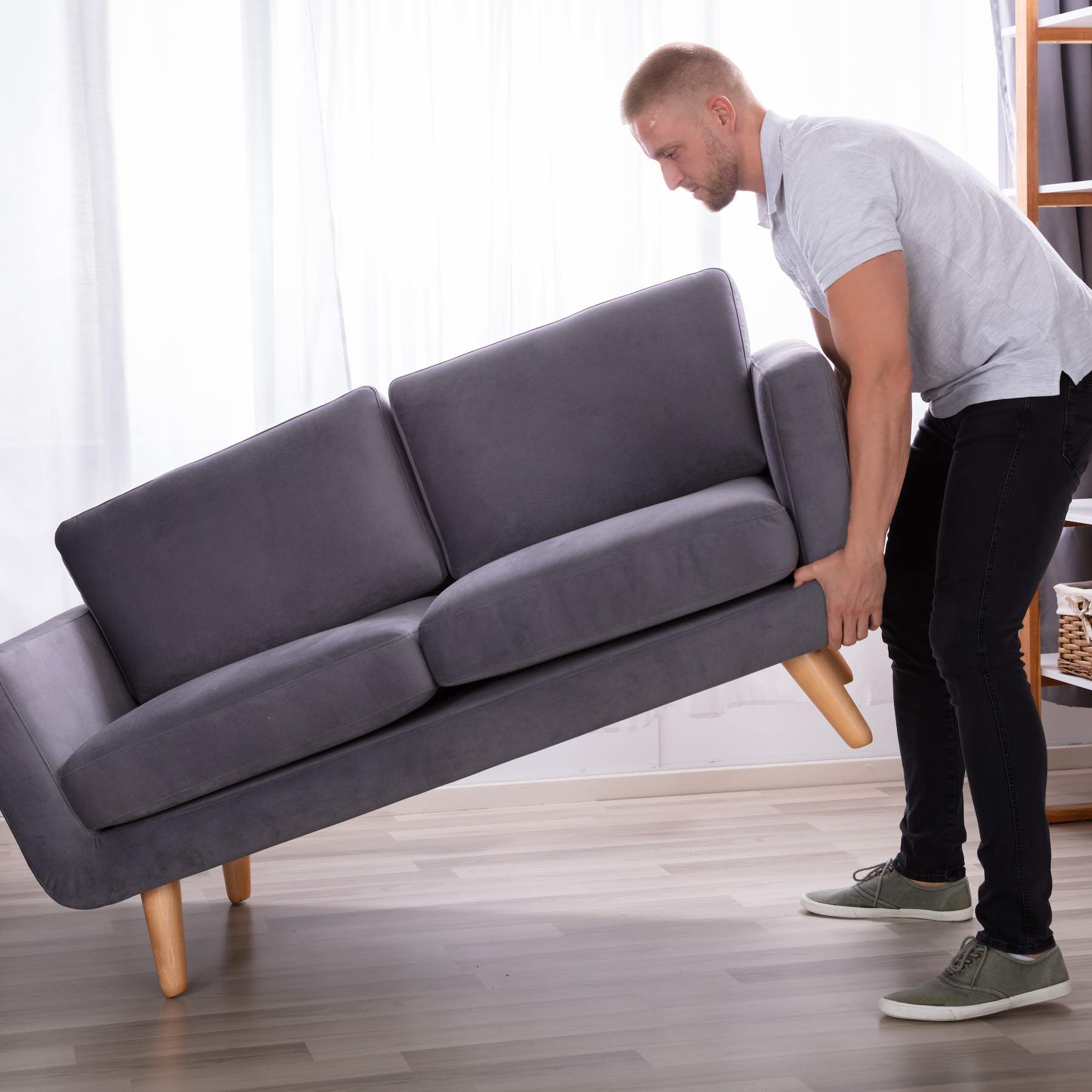 Side View Of A Young Man Lifting Sofa At Home