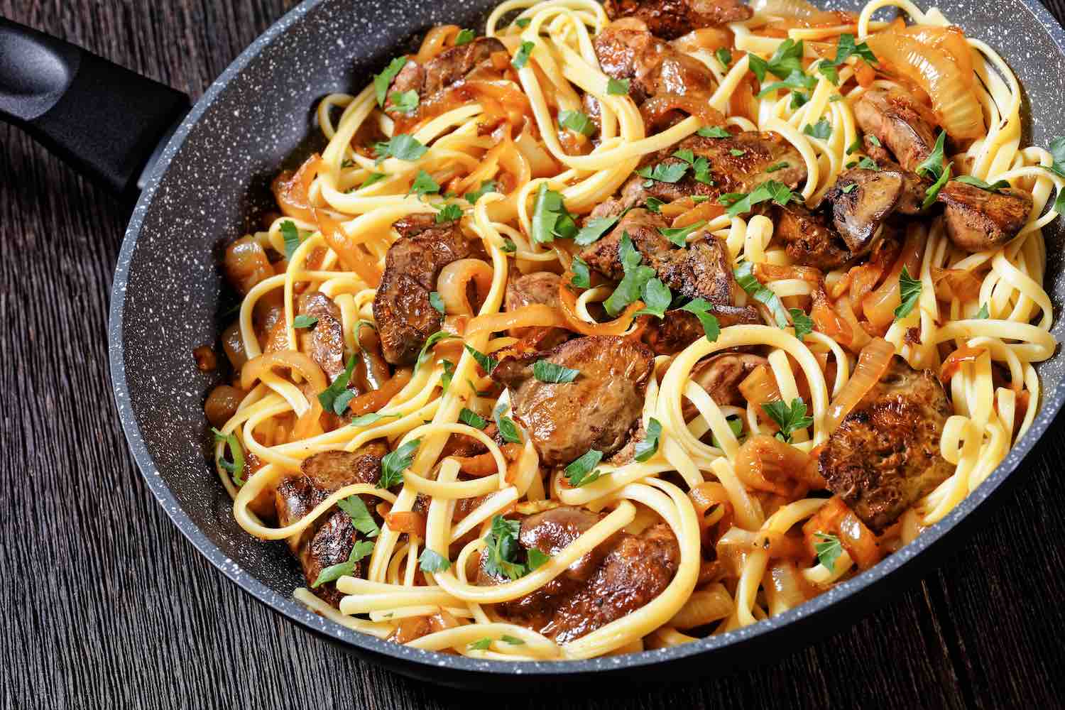 pasta linguine with fried chicken liver, caramelized onion and parsley in a skillet, horizontal view from above, close-up, Italian cuisine