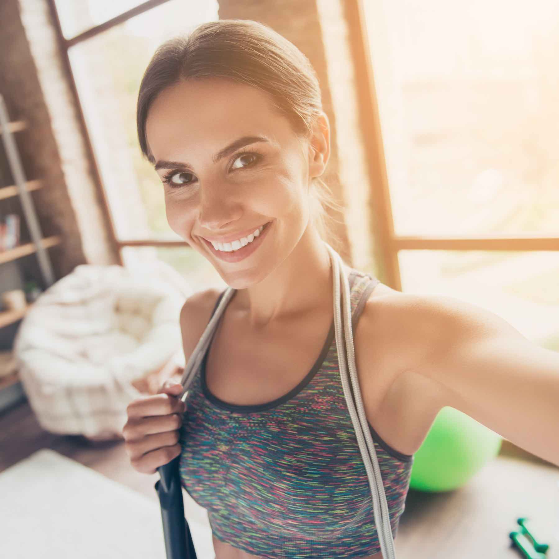 Close up portrait of excited active attractive cheerful beautiful strong skinny with beaming smile wearing sportive top with jump-rope on shoulders taking selfie for social-networks