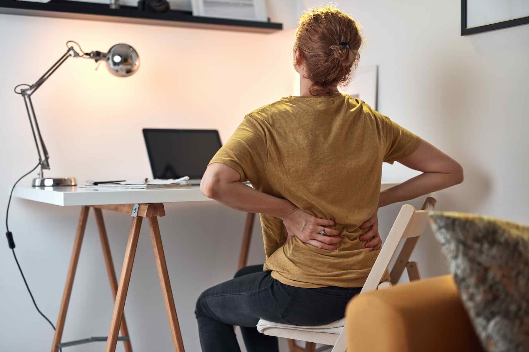 Woman working on a laptop at home and having problems with hips, back and stomack ache.
