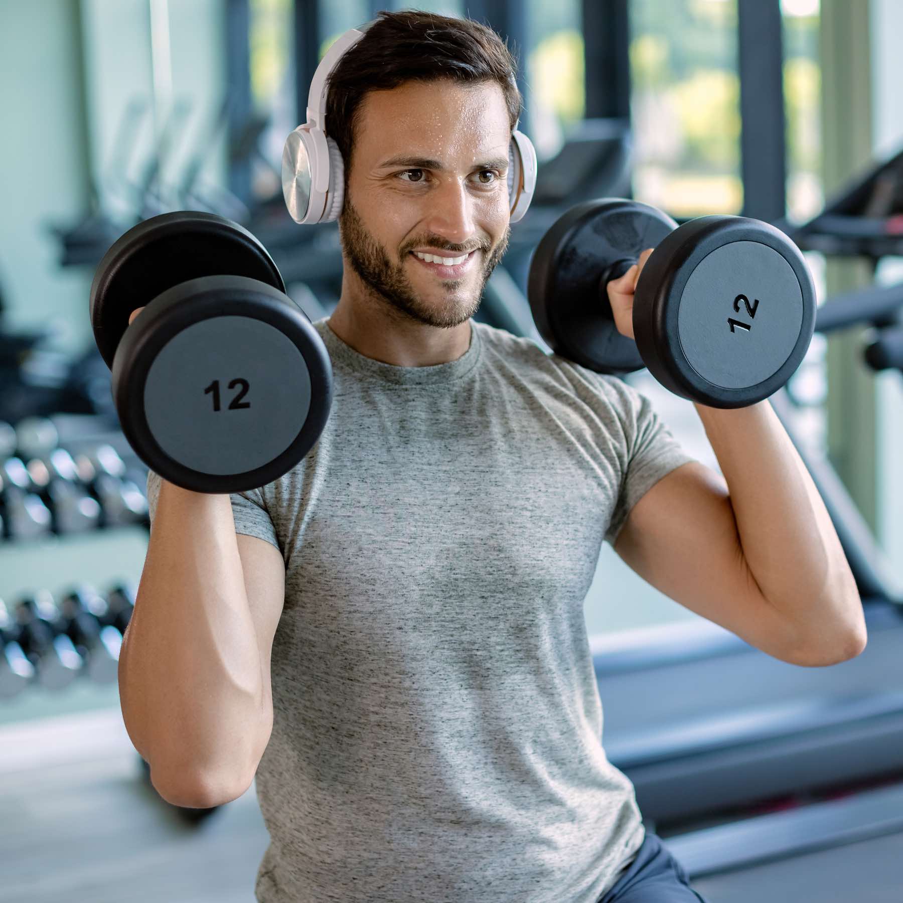 Young happy athletic man having weight training at health club. Happy athlete exercising with hand weights during cross training in a gym.