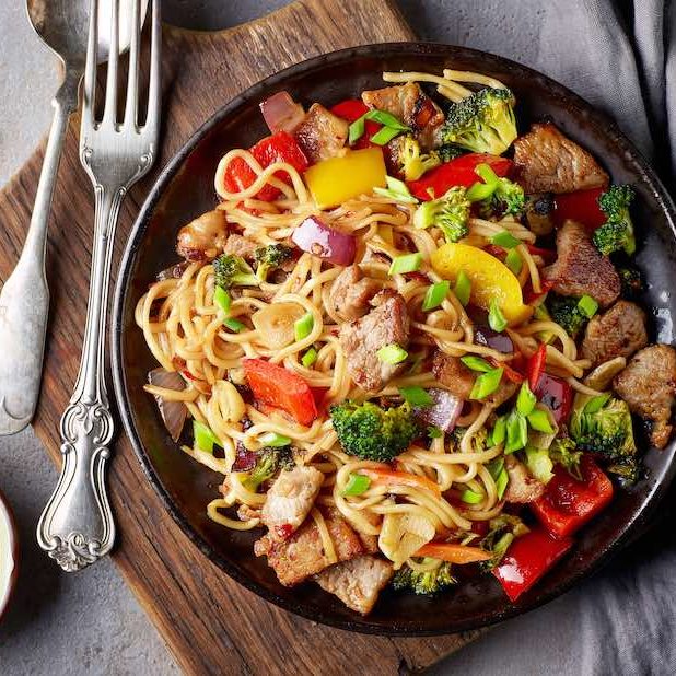 Noodles with meat and vegetables on grey table, top view